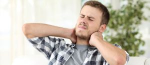 man suffering neck pain sitting on a sofa
